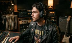 A person wearing black Marshall headphones against a moody studio background.