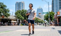 Person wearing over-ear Soundcore headphones walking outdoors on a sunny Texas day.